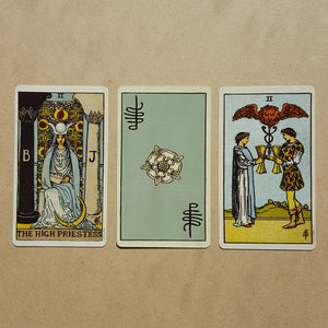  Three tarot cards, left to right:  The High Priestess, a back of a card featuring Pixie's signature and a white Tudor style rose on light blue, two of cups.