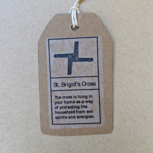 Detail of kraft paper hang tag that accompanies each cross.  Top has black drawing of the cross, bottom text reads "The cross is hung in your home as a way of protecting the household from evil spirits and energies." in black ink.