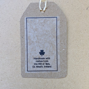 Detail from back of kraft paper hang tag that accompanies each cross.  Small clover and text that reads "Handmade with rushes from the Hill of Tara, Co. Meath, Ireland." in black ink.
