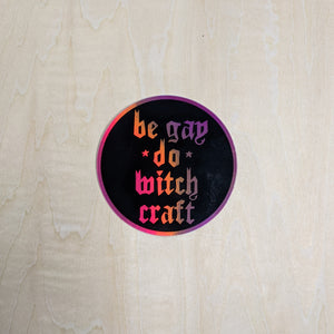 Black round sticker by Midge Blitz with holographic "be gay do witch craft" in the center.  Holograph flashes from orange, to pink, to purple depending on the lighting & angle  available at Coyote Supply Co, a zero waste witch store in Midtown Reno, Nevada that is BIPOC owned