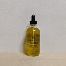 Load image into Gallery viewer, Glass bottle with black dropper lid containing golden multi use oil by Motherland Essentials reads &quot;teakwood&quot; in black block letters available at Coyote Supply Co, a zero waste witch store in Midtown Reno, Nevada that is BIPOC owned