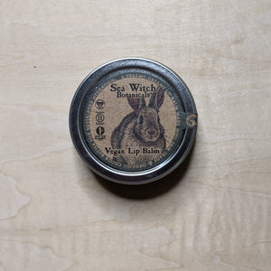Round metal tin with round kraft paper label featuring a blue boarder & a fluffy bunny containing vegan lip balm by Sea Witch Botanicals available at Coyote Supply Co, a zero waste witch store in Midtown Reno, Nevada that is BIPOC owned