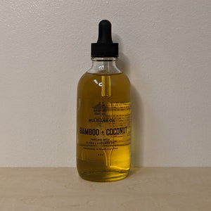 Glass bottle with black dropper lid containing golden multi use oil by Motherland Essentials reads "bamboo + coconut" in black block letters available at Coyote Supply Co, a zero waste witch store in Midtown Reno, Nevada that is BIPOC owned