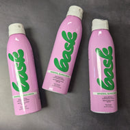 Three pink Bask sunscreen bottle with a white spray cap on a dark grey background.

The bottle reads:
Bask, Mineral Sunscreen, non-aerosol continuous spray, broad spectrum SPF 50, water resistant. 

Sold at Coyote Supply Co a BIPOC and LGBTQIA+ owned zero waste witch store in Reno Nevada 