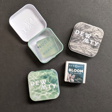 Load image into Gallery viewer, The DEW MTY Bloom jelly serum bar alongside it's packaging options of a paper wrap or metal case in green or grey. Sold at Coyote Supply Co a BIPOC and LGBTQIA+ owned zero waste witch store in Reno Nevada