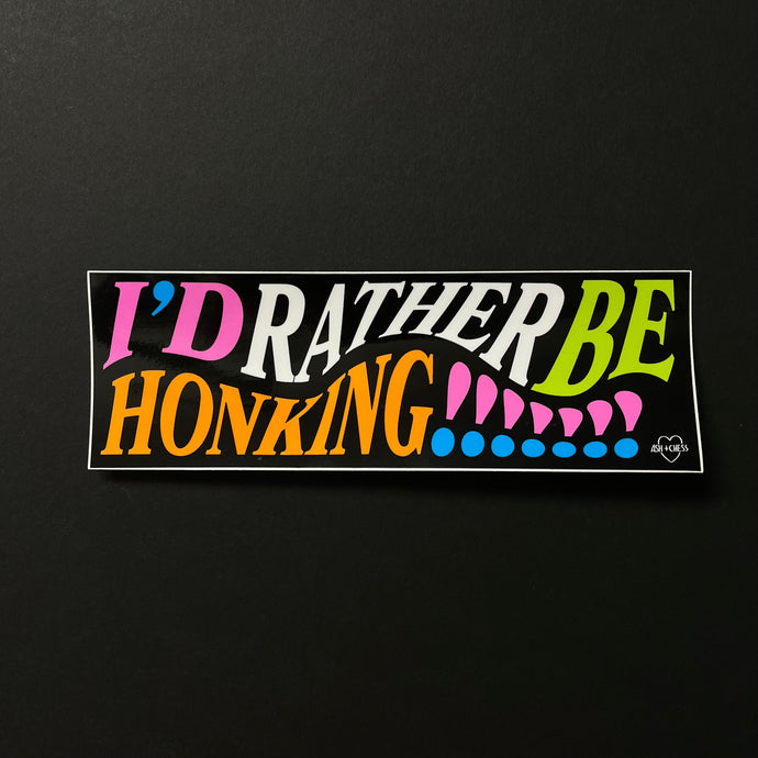 A black bumper sticker with multi color text that reads: I'd rather be honking!!!!!!!  Sold at Coyote Supply Co a BIPOC and LGBTQIA+ owned zero waste witch store in Reno Nevada 