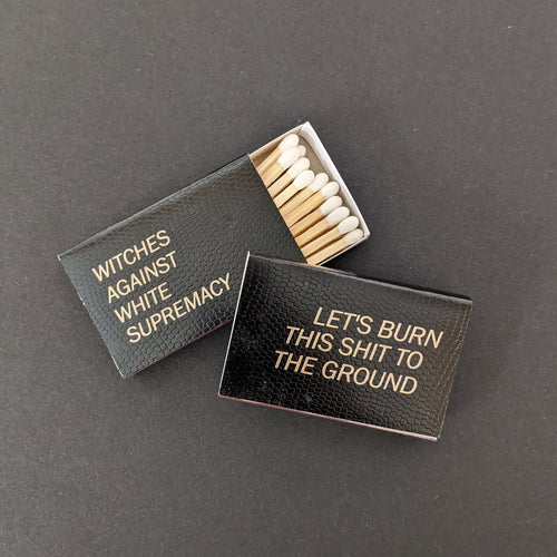 Two black matchboxes on a black background. The boxes have a scale texture and gold foil lettering. The left box reads: 