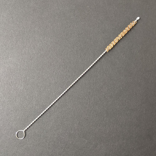 A boba straw brush comprised of a twisted metal and natural brown bristles on a black background.  Sold at Coyote Supply Co a BIPOC and LGBTQIA+ owned zero waste witch store in Reno Nevada 