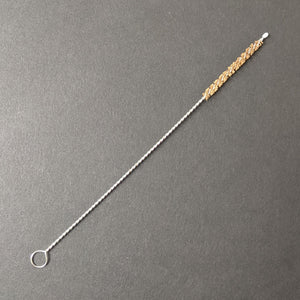 A boba straw brush comprised of a twisted metal and natural brown bristles on a black background.  Sold at Coyote Supply Co a BIPOC and LGBTQIA+ owned zero waste witch store in Reno Nevada 