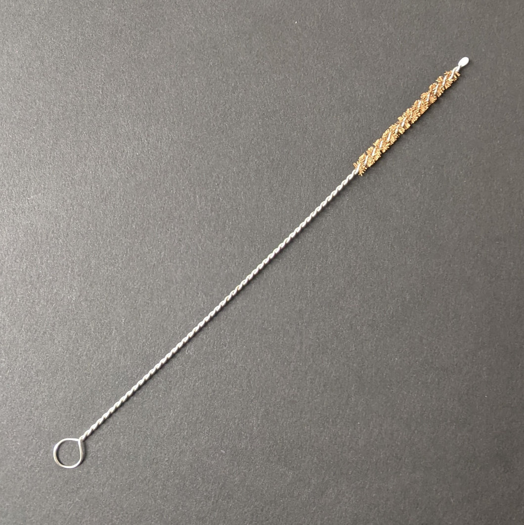 A boba straw brush comprised of a twisted metal and natural brown bristles on a black background.  Sold at Coyote Supply Co a BIPOC and LGBTQIA+ owned zero waste witch store in Reno Nevada 