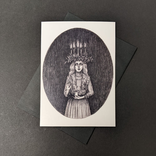 A white card with a monochrome illustration of Santa Lucia by Caitlin McCathy against a black envelope. Sold at Coyote Supply Co a BIPOC and LGBTQIA+ owned zero waste witch store in Reno Nevada 