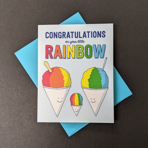 A light blue card with an illustration of a snow cone family that reads Congratulations on your little Rainbow. Sold at Coyote Supply Co a BIPOC and LGBTQIA+ owned zero waste witch store in Reno Nevada 