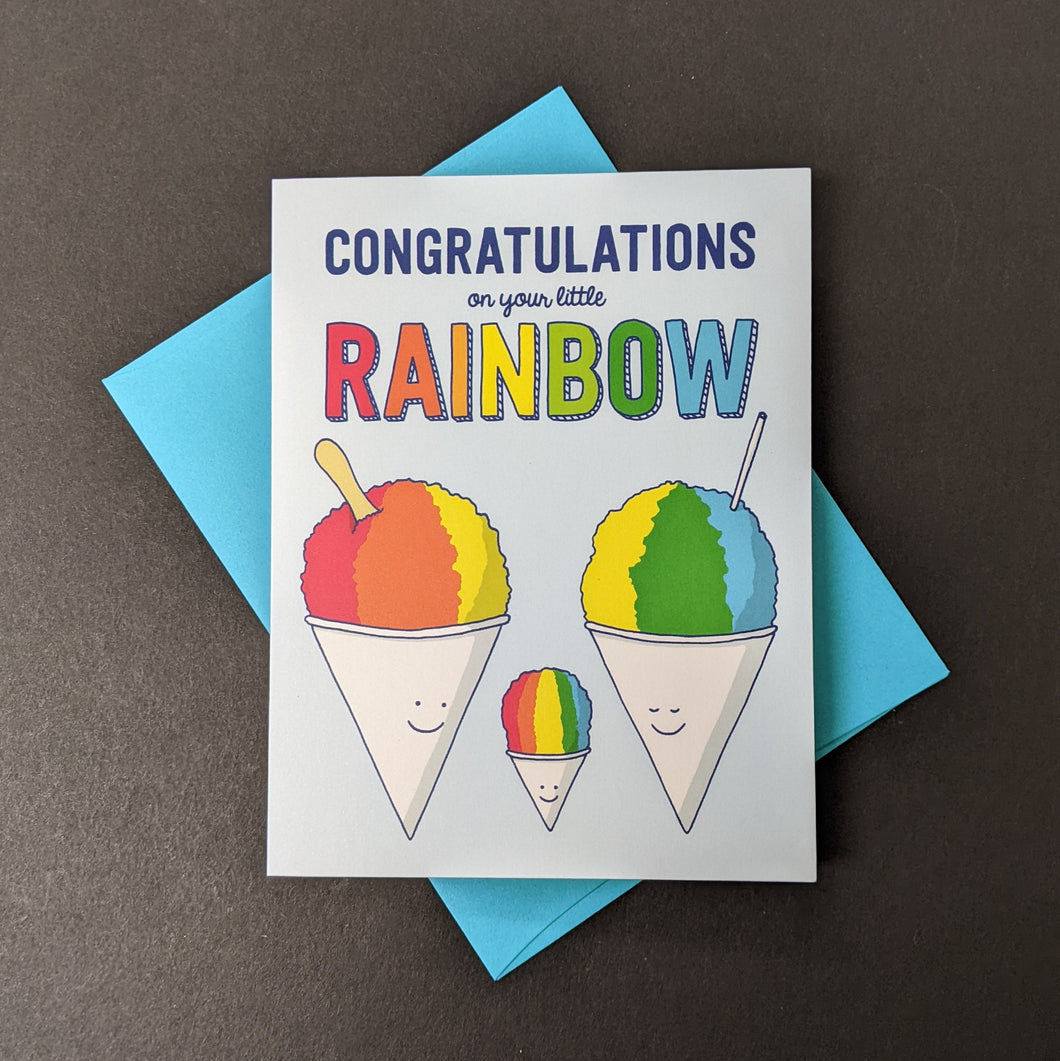 A light blue card with an illustration of a snow cone family that reads Congratulations on your little Rainbow. Sold at Coyote Supply Co a BIPOC and LGBTQIA+ owned zero waste witch store in Reno Nevada 