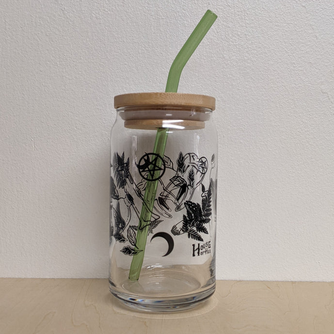 A glass can style cup with bamboo lid and green glass straw. The cup has many witchy elements wrapping around the entire glass. Sold at Coyote Supply Co a BIPOC and LGBTQIA+ owned zero waste witch store in Reno Nevada 