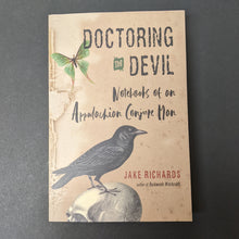 Load image into Gallery viewer, A tan book cover with images of a moth and crow atop a skull that reads Doctoring the Devil Notebooks of an Appalachian Conjure Man by Jake Richards. Sold at Coyote Supply Co a BIPOC and LGBTQIA+ owned zero waste witch store in Reno Nevada
