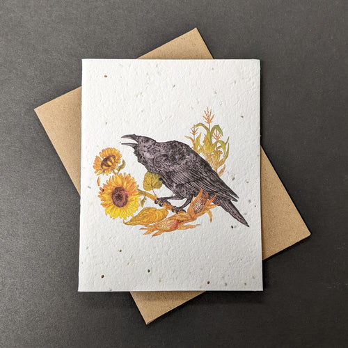 A white seed paper card with a brown craft envelope behind it on a black background. The card has a watercolor style illustration of a raven perche

Sold at Coyote Supply Co a BIPOC and LGBTQIA+ owned zero waste witch store in Reno Nevada on sunflowers with corn plants behind it.
