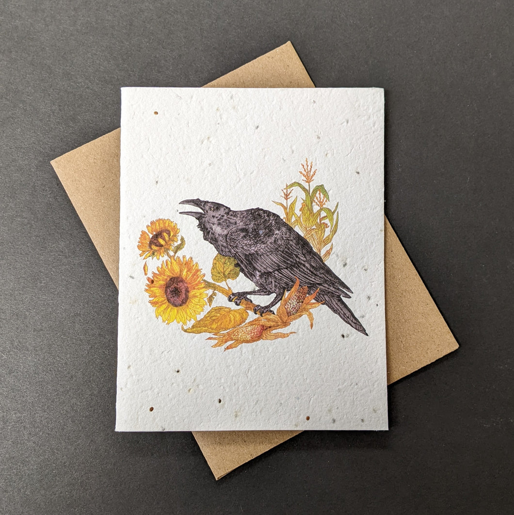A white seed paper card with a brown craft envelope behind it on a black background. The card has a watercolor style illustration of a raven perche

Sold at Coyote Supply Co a BIPOC and LGBTQIA+ owned zero waste witch store in Reno Nevada on sunflowers with corn plants behind it.