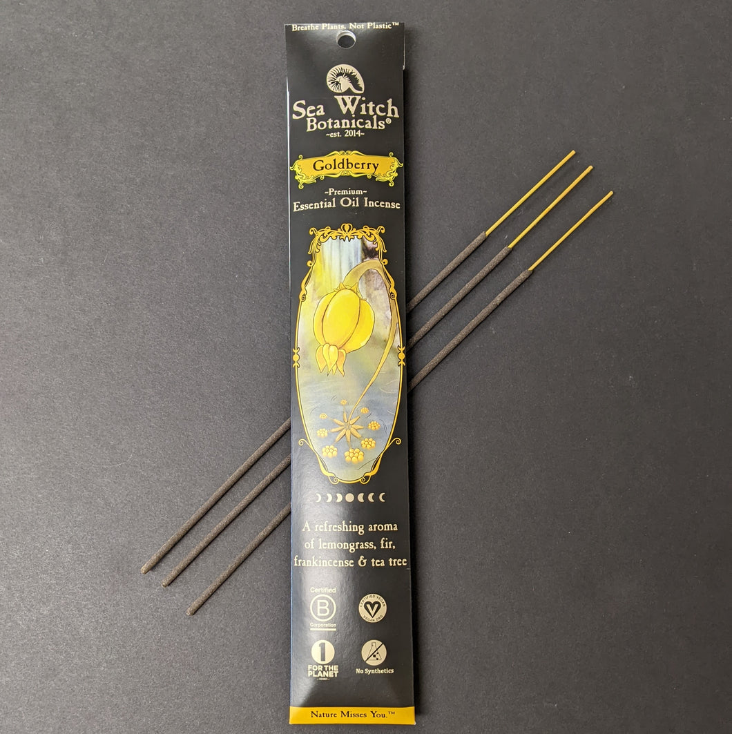 A glossy black cardboard envelope of incense. The center has an illustration of a gold berry in a forest. The box reads