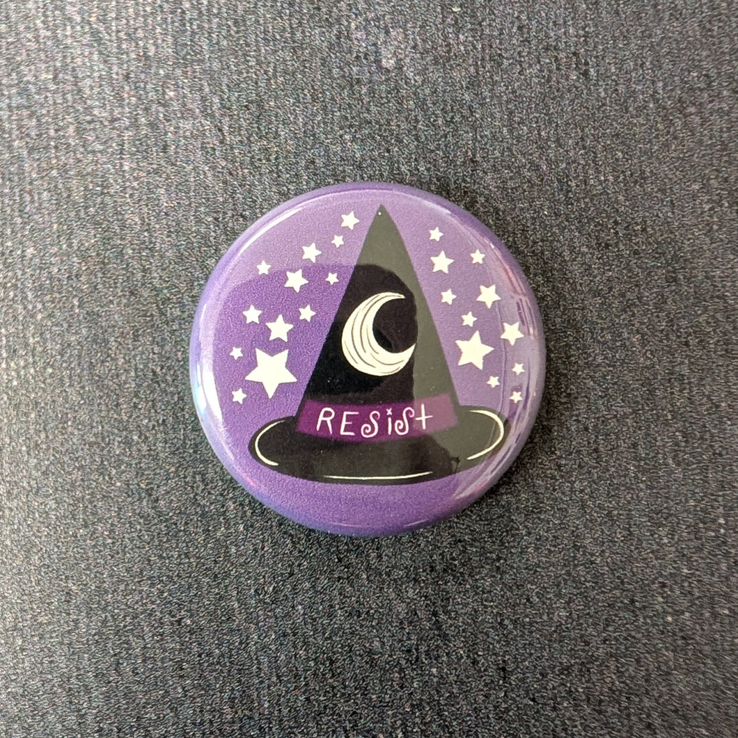 A glossy purple button with white stars and a black witch hat with a dark purple band illustration. The band of the at says 