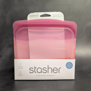 A clear pink silicone sandwich bag with a white cardboard band around it. The band has grey text that reads:
SANDWICH
easy open pinch-loc seal
stasher
save what matters
plastic free
cook it freeze it store it"
Sold at Coyote Supply Co a BIPOC and LGBTQIA+ owned zero waste witch store in Reno Nevada