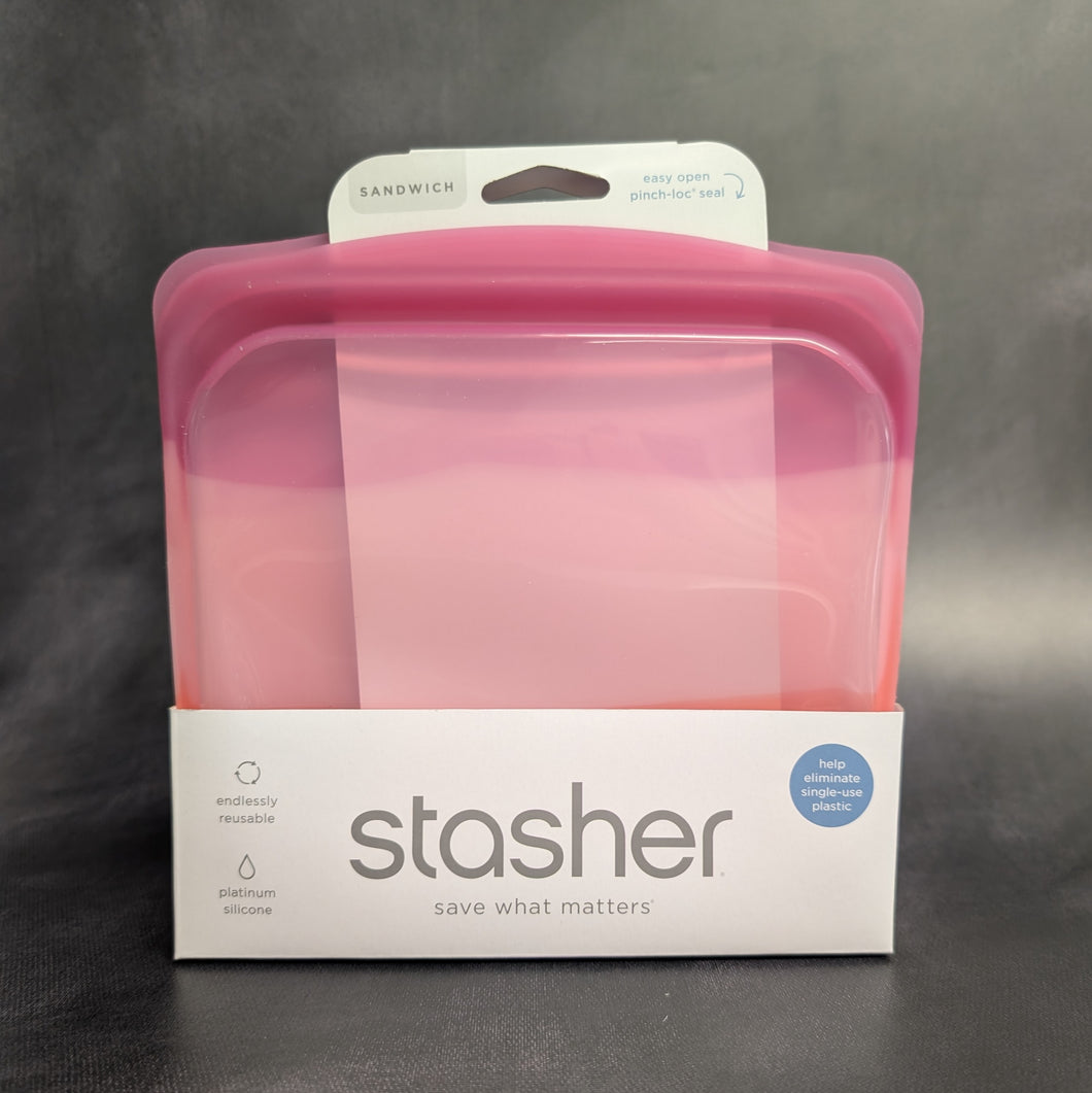 A clear pink silicone sandwich bag with a white cardboard band around it. The band has grey text that reads:
SANDWICH
easy open pinch-loc seal
stasher
save what matters
plastic free
cook it freeze it store it