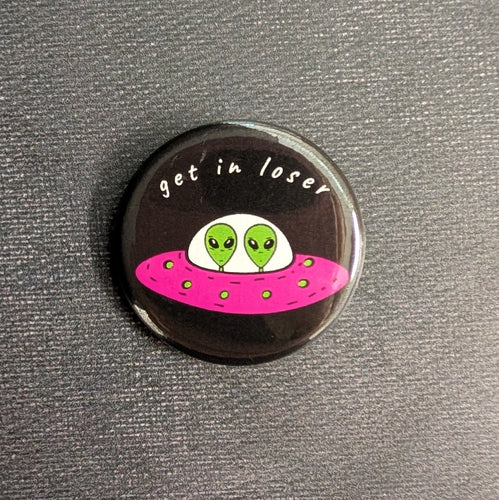 A black button with an illustration of two aliens in a pink saucer style UFO with white text above them that reads 