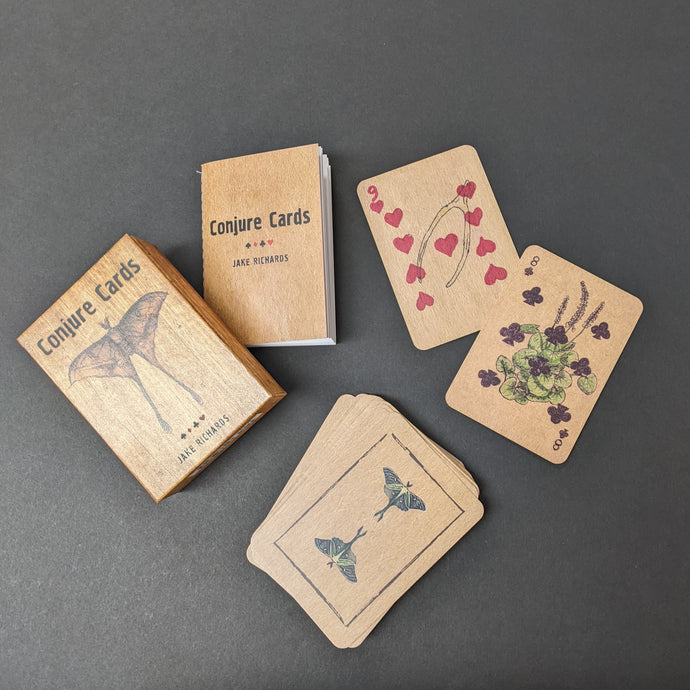 The box and guide book for Conjure Cards by Jake Richards on a black background with an assortment of the brown playing card styled conjure cards. Sold at Coyote Supply Co a BIPOC and LGBTQIA+ owned zero waste witch store in Reno Nevada
