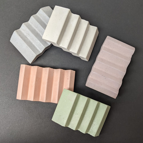 Six zig zag shaped concrete soap dishes. Going clockwise the colors are white, purple, green, orange, and grey.  Sold at Coyote Supply Co a BIPOC and LGBTQIA+ owned zero waste witch store in Reno Nevada 
