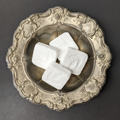 four white cubed cleaning bombs by MamaSuds in a silver plate. Sold at Coyote Supply Co a BIPOC and LGBTQIA+ owned zero waste witch store in Reno Nevada