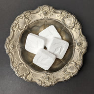 four white cubed cleaning bombs by MamaSuds in a silver plate. Sold at Coyote Supply Co a BIPOC and LGBTQIA+ owned zero waste witch store in Reno Nevada
