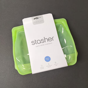 A clear green silicone standing bag with a white cardboard band around it. The band has grey text that reads:
STAND-UP MEGA
3077ml / 104 fl oz
stasher
save what matters
plastic free
cook it freeze it store it"
Sold at Coyote Supply Co a BIPOC and LGBTQIA+ owned zero waste witch store in Reno Nevada