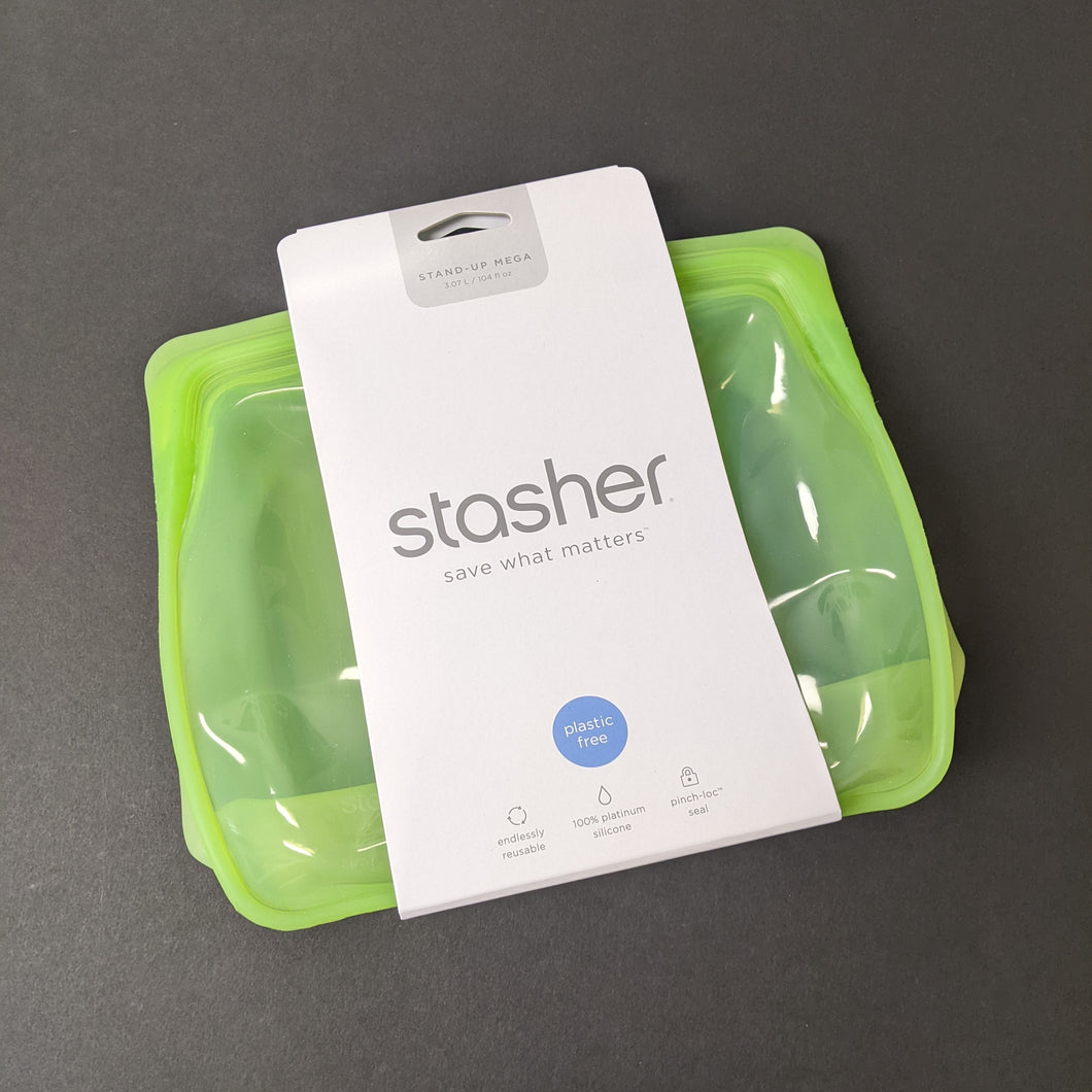 A clear green silicone standing bag with a white cardboard band around it. The band has grey text that reads:
STAND-UP MEGA
3077ml / 104 fl oz
stasher
save what matters
plastic free
cook it freeze it store it