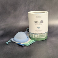 A blue colored saalt menstrual disc on it's cool colored cloth carrying bag next to it's packaging cylinder on a dark background. The light colored packaging cylinder has grey text that reads:
Size Regular
Coastal Blue
Saalt
menstrual disc
Period care simplified
Made in the USA

This item is sold at Coyote Supply Co a BIPOC and LGBTQIA+ owned zero waste witch store in Reno Nevada