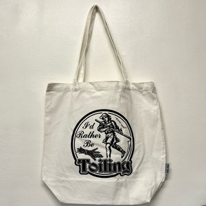 A white tote bag with a black screen printed design of a medieval peasant that reads I'd Rather Be Toiling.  Sold at Coyote Supply Co a BIPOC and LGBTQIA+ owned zero waste witch store in Reno Nevada 