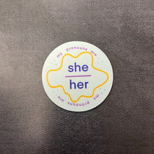 Load image into Gallery viewer, Round pronoun label sticker for she/her on a dark background.

This item is sold at Coyote Supply Co a BIPOC and LGBTQIA+ owned zero waste witch store in Reno Nevada