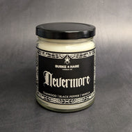 An 8oz candle with a black metal lid and a black label that reads: Burke & Hare Co Nevermore a poetic blend of teakwood, tobacco, vanilla, aand black pepper.  Sold at Coyote Supply Co a BIPOC and LGBTQIA+ owned zero waste witch store in Reno Nevada 
