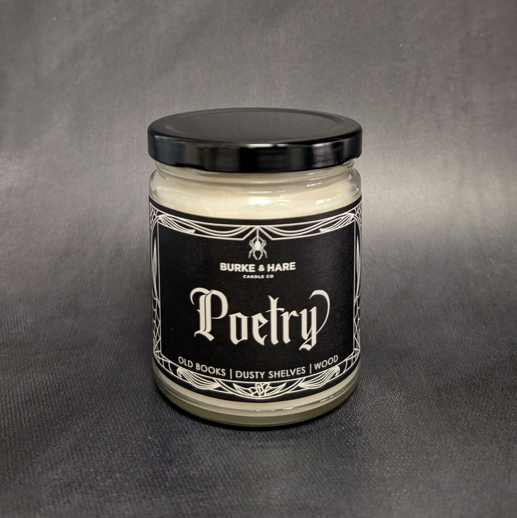 An 8oz candle with a black metal lid and a black label that reads: Burke & Hare Co Poetry a cozy blend of dusty books, wooden shelves, and leather. Sold at Coyote Supply Co a BIPOC and LGBTQIA+ owned zero waste witch store in Reno Nevada 