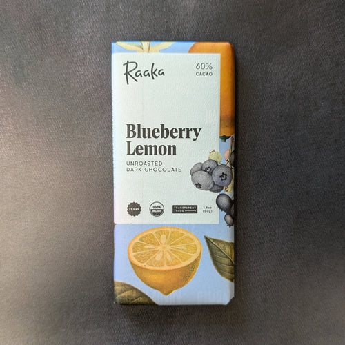 A light blue paper wrapped chocolate bar, the paper has a white square with black text about the bar and an illustration of lemons and blueberries. The text on the bar reads 