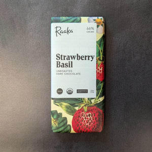 A chocolate bar wrapped in a light yellow paper wrapper with illustrations of strawberry and basil leaves, in the center is a white square with black text. The text reads "Raaka 66% CACAO
Strawberry
Basil
UNROASTED
DARK CHOCOLATE"
Sold at Coyote Supply Co a BIPOC and LGBTQIA+ owned zero waste witch store in Reno Nevada