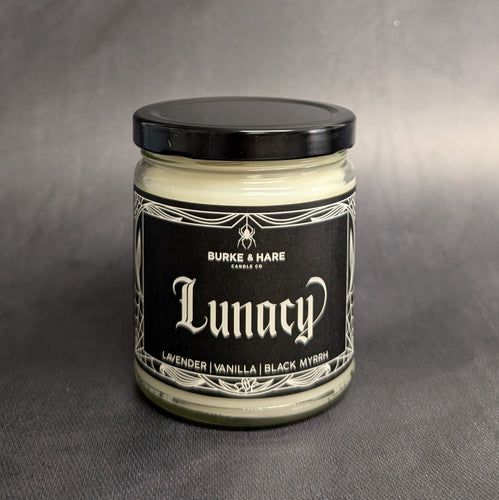 An 8oz vegan candle with a black metal lid and black label that reads Burke & Hare Co Lunacy a calming blend of wild lavender vanilla, and black myrrh.  Sold at Coyote Supply Co a BIPOC and LGBTQIA+ owned zero waste witch store in Reno Nevada 