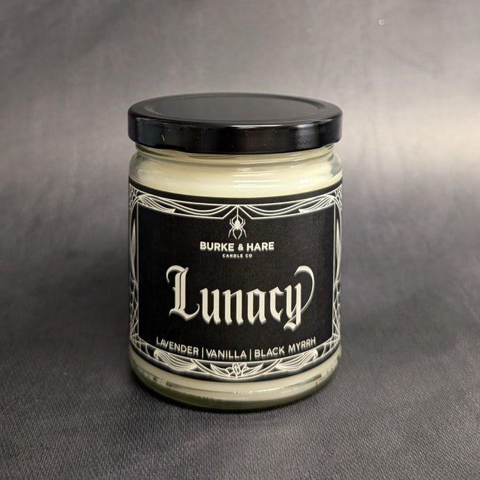 An 8oz vegan candle with a black metal lid and black label that reads Burke & Hare Co Lunacy a calming blend of wild lavender vanilla, and black myrrh.  Sold at Coyote Supply Co a BIPOC and LGBTQIA+ owned zero waste witch store in Reno Nevada 
