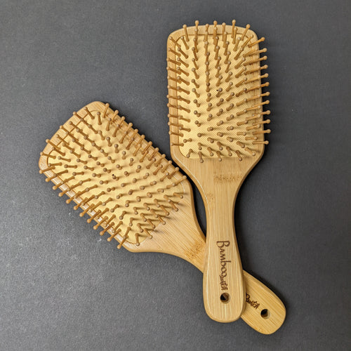 Two bamboo hair brushes on a black background.  Sold at Coyote Supply Co a BIPOC and LGBTQIA+ owned zero waste witch store in Reno Nevada 