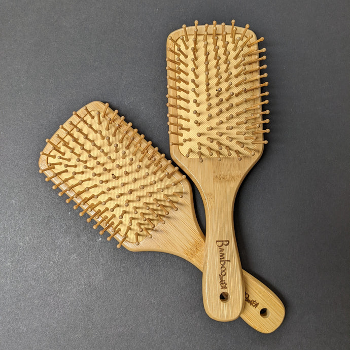 Two bamboo hair brushes on a black background.  Sold at Coyote Supply Co a BIPOC and LGBTQIA+ owned zero waste witch store in Reno Nevada 