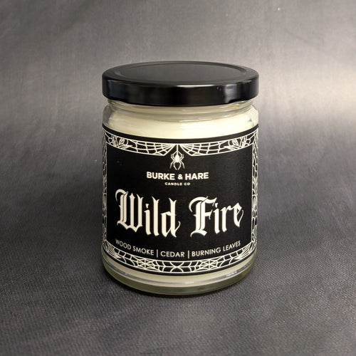 An 8oz vegan candle with a black metal lid and black label that reads Burke & Hare Co Wildfire woodsmoke, burning leaves, and a hint of autumn spice.  Sold at Coyote Supply Co a BIPOC and LGBTQIA+ owned zero waste witch store in Reno Nevada 