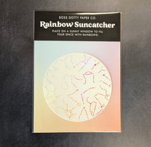 Load image into Gallery viewer, A suncatcher sticker in its packaging pictured on a dark background. The packaging is a flat cardboard square with rainbow pastel gradient and a black band at the top with white text.
The text reads:
BOSS DOTTY PAPER CO.
Rainbow Suncatcher
Place on a sunny window to fill
your space with rainbows!

This item is sold at Coyote Supply Co a BIPOC and LGBTQIA+ owned zero waste witch store in Reno Nevada