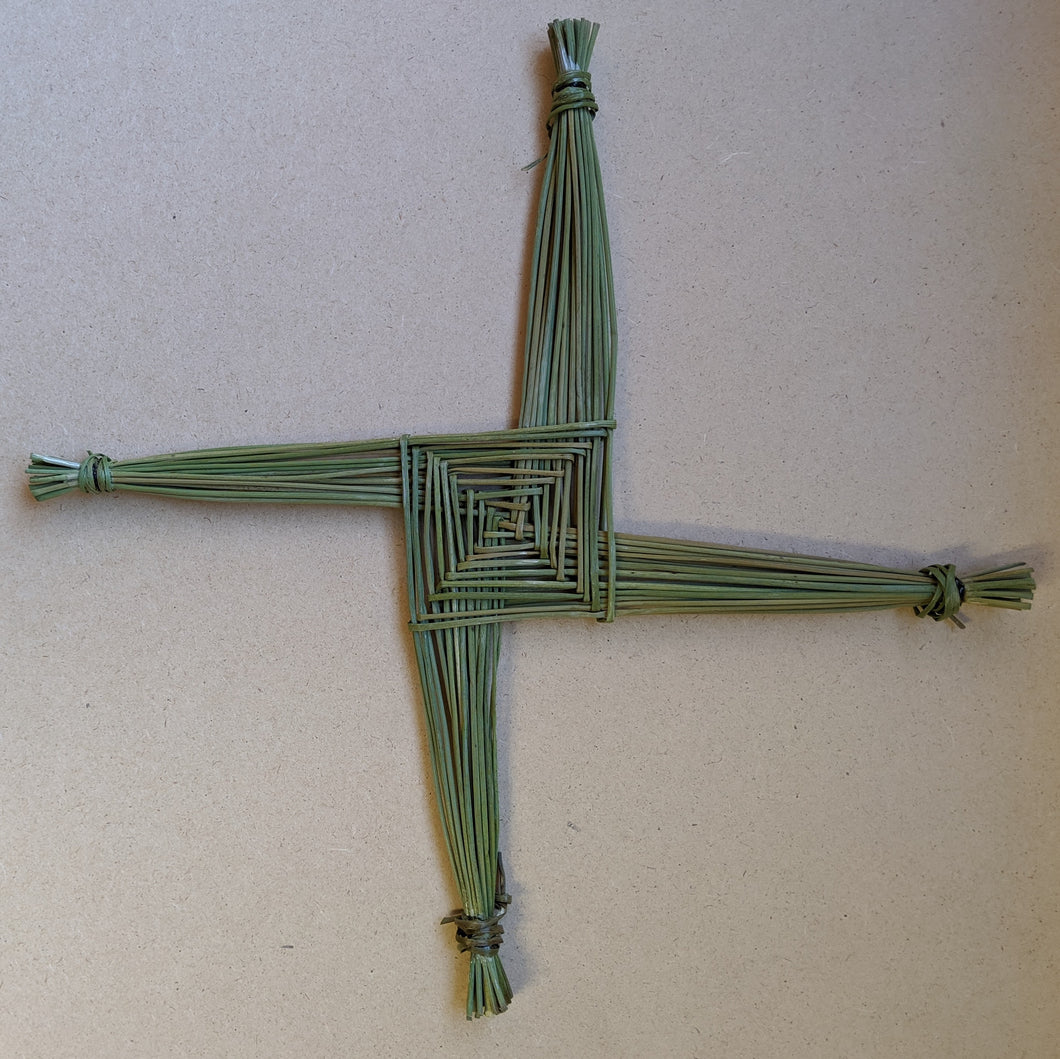 A squared off cross, called a Brigid's Cross, made of green rushes on particle board background  available at Coyote Supply Co, a zero waste witch store in Midtown Reno, Nevada that is BIPOC owned