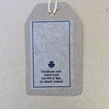 Load image into Gallery viewer, Detail from back of kraft paper hang tag that accompanies each cross.  Small clover and text that reads &quot;Handmade with rushes from the Hill of Tara, Co. Meath, Ireland.&quot; in black ink.