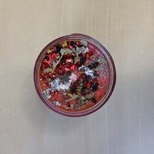 Load image into Gallery viewer, Red soy wax candle topped with confetti, herbs, glitter, and silver leaf by Firme Arte available at Coyote Supply Co, a zero waste witch store in Midtown Reno, Nevada that is BIPOC owned