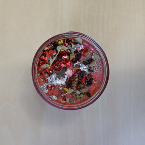 Red soy wax candle topped with confetti, herbs, glitter, and silver leaf by Firme Arte available at Coyote Supply Co, a zero waste witch store in Midtown Reno, Nevada that is BIPOC owned