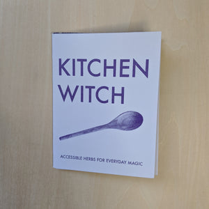 Purple text on lavender paper reads "Kitchen Witch Accessible Herbs for Everyday Magic" and features a photo of a wooden spoon  by Snake Hair Press available at Coyote Supply Co, a zero waste witch store in Midtown Reno, Nevada that is BIPOC owned